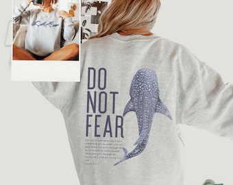 May include: A gray sweatshirt with a whale shark graphic and the text "DO NOT FEAR" printed on the back. The text below the graphic reads "for I have redeemed you, I have summoned you by name; you are mine. When you pass through the waters, I will be with you; and when you go through the rivers, they will not sweep over you. Isaiah 43:1-2"
