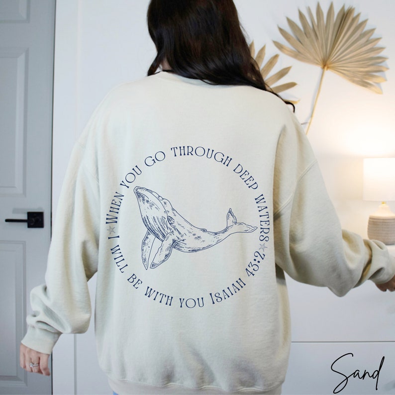 May include: A beige sweatshirt with a blue whale graphic and the text "When you go through deep waters I will be with you Isaiah 43:2" printed on the back.