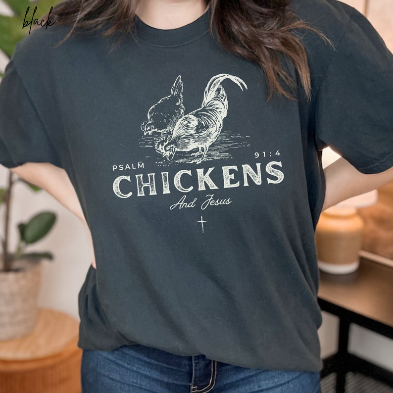 May include: A dark gray t-shirt with a white graphic of two chickens and the text "Psalm 91:4 Chickens And Jesus" with a small cross underneath.