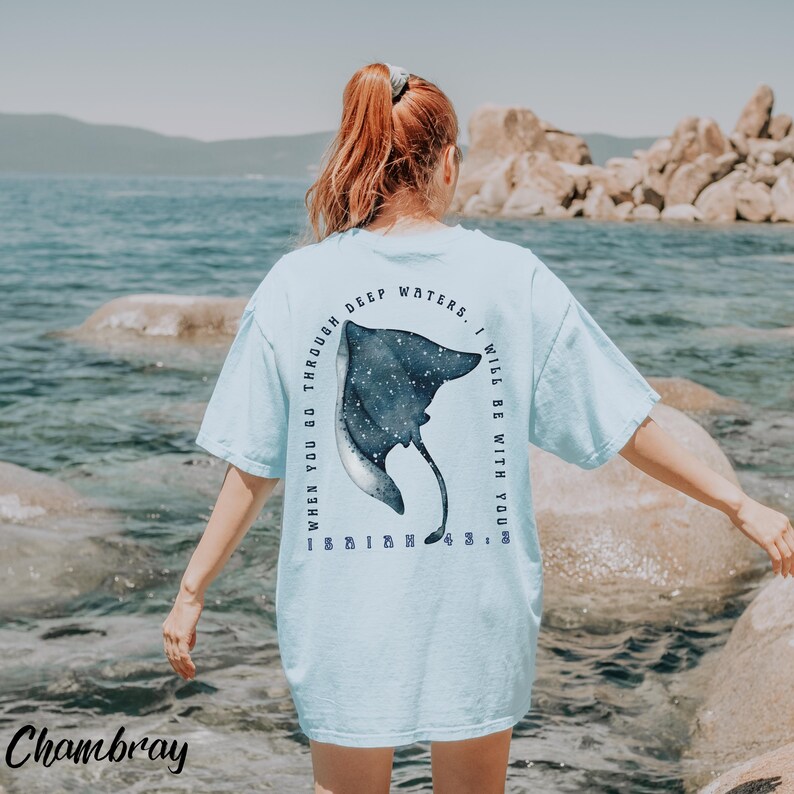 May include: Light blue t-shirt with a watercolor-style stingray design on the back. The text reads "WHEN YOU GO THROUGH DEEP WATERS, I WILL BE WITH YOU." The word "Chambray" is printed at the bottom.