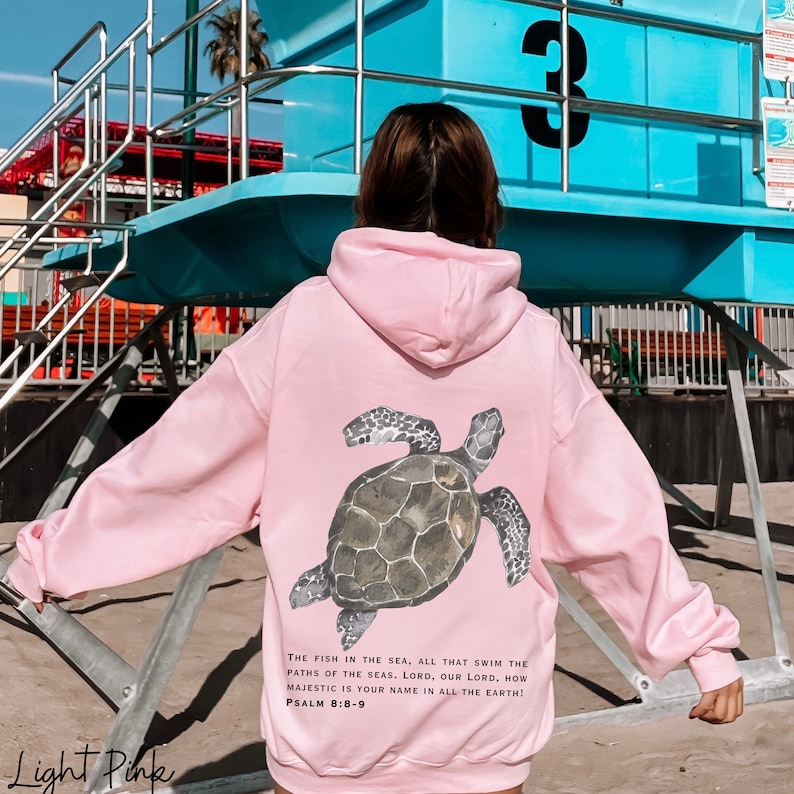 May include: Light pink hooded sweatshirt with a sea turtle graphic on the back. The text "THE FISH IN THE SEA, ALL THAT SWIM THE PATHS OF THE SEAS. LORD, OUR LORD, HOW MAJESTIC IS YOUR NAME IN ALL THE EARTH! PSALM 8:8-9" is printed below the graphic.