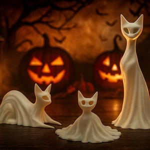 May include: Three white cat figurines in various poses, with a Halloween theme. The cats are in a spooky setting with carved pumpkins and candles in the background. The figurines are made of a smooth material.