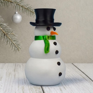 The same snowman stash ornament shown from a gentle angle, highlighting its pitted, snow-like texture and shiny green scarf.