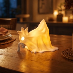 A single glowing chicken ghost figure leans forward, pulling a ghostly worm from the ether. Resting on a table in a cozy dining room, this macabre desk bird operates as a cute spooky led lamp. Part of the glowing chicken ghost trio, it brings weirdcore room decor and cozy witchy accents to life. This funny glowing fowl is an excellent pastel goth oddity, fitting perfectly as goblincore dopamine gifts or fairy garden items. Add an alt dark aesthetic to your home with this whimsigoth decor.