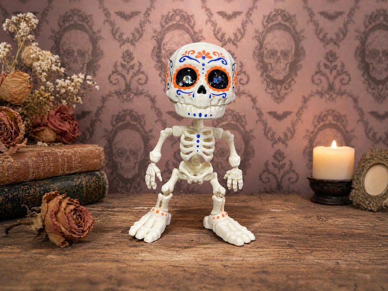 A close-up of the blue and orange patterned articulated skeleton standing proudly on a wooden dresser. This specific colorway perfectly captures the vibrant calavera art style, making this sugar skull figure a standout weirdcore accessory. Acting as an ADHD fidget tool for office or home, this tactile sensory item decor is the ultimate fun dopamine decor. A ready to ship goth gift and creepy cute pastel goth desk buddy for any alternative space.