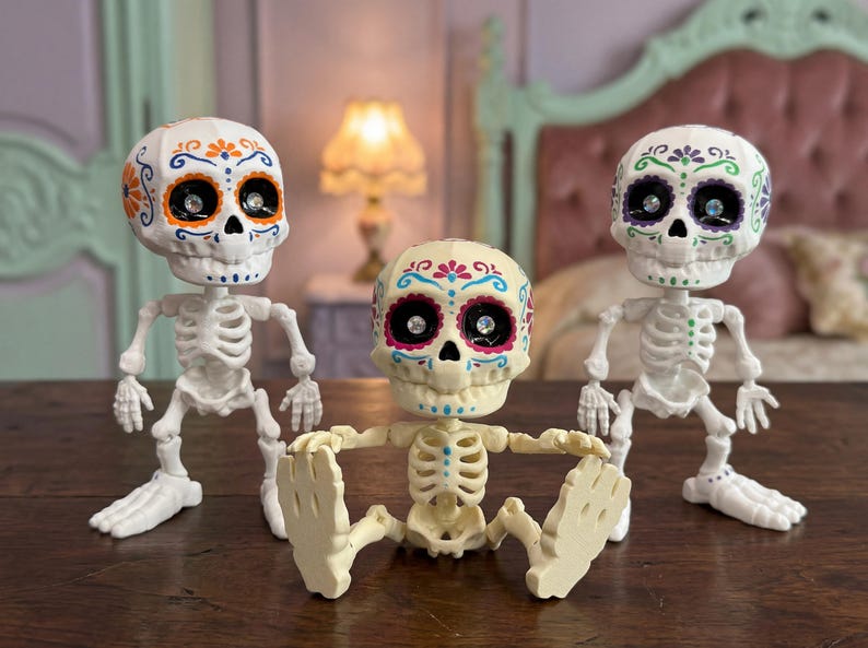 Three articulated skeleton toys displayed side by side in a cozy pastel goth bedroom setting. The center skeleton is sitting while the two outer figures stand, highlighting the posable nature of this ADHD fidget tool for office or home. A brilliant pastel goth vibe emanates from these vibrant calavera art pieces. An ideal witchy gift for friend or a quirky gift for adhd friend needing a fun dopamine decor element and weirdcore accessory.