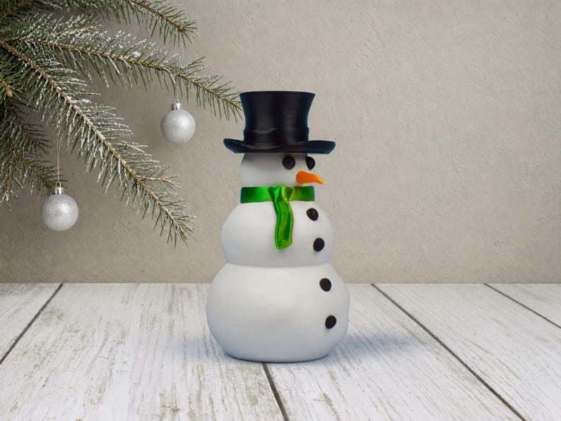 The same snowman stash ornament shown from a gentle angle, highlighting its pitted, snow-like texture and shiny green scarf.