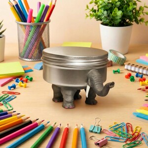 Organized chaos on a desk showing the elephant tin with paperclips and small office supplies. It perfectly captures the weirdcore aesthetic room decor vibe. A practical yet fun made to order oddities container that acts as a popular adhd friendly workspace decor piece. Ideal for those wanting to buy elephant novelty tin organizer storage.