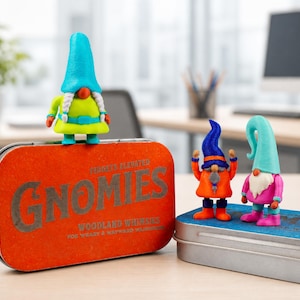 May include: Three small gnome figurines standing on two rectangular metal tins. One gnome has a bright blue hat and lime green outfit. The other two have blue and orange hats with pink and orange outfits. The orange tin features the text GNOMIES.