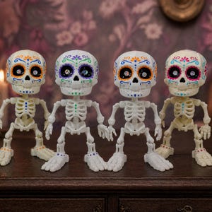 Four vibrant calavera art pieces standing side by side against a striking purple wallpaper background. This lineup displays the beautiful color variations of this creepy cute pastel goth desk buddy. As an articulated skeleton ADHD fidget tool for office spaces, it brings a massive pastel goth vibe to any maximalist cubicle. A fantastic tactile sensory item and ready to ship goth gift that doubles as incredibly fun dopamine decor for your space.