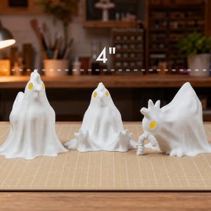 An informative graphic showing the glowing chicken ghost trio lined up, with a measurement overlay indicating heights range from 3 to 4 inches. These macabre desk bird figures act as a cute spooky led lamp set, bringing weirdcore room decor and cozy witchy accents to any shelf. Each funny glowing fowl is a unique pastel goth oddity. Perfect for alt dark aesthetic displays, these whimsigoth gifts deliver goblincore dopamine and double as beautifully eerie indoor fairy garden items.