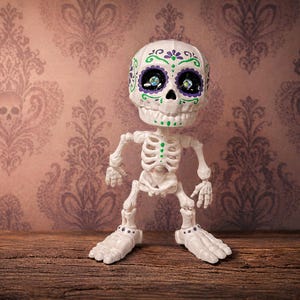 A single creepy cute statue of an articulated skeleton standing confidently in a jaunty pose against a pastel goth wallpaper background. This office desk buddy is designed as a tactile sensory item for satisfying engagement. The sugar skull figure details pop beautifully, making it an excellent weirdcore accessory and ready to ship goth gift. Perfect as an ADHD fidget tool for office environments or as maximalist cubicle dopamine decor.