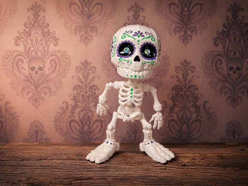 A single creepy cute statue of an articulated skeleton standing confidently in a jaunty pose against a pastel goth wallpaper background. This office desk buddy is designed as a tactile sensory item for satisfying engagement. The sugar skull figure details pop beautifully, making it an excellent weirdcore accessory and ready to ship goth gift. Perfect as an ADHD fidget tool for office environments or as maximalist cubicle dopamine decor.