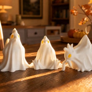 A trio of funny glowing fowl statues, our glowing chicken ghost trio, sits bathed in golden late afternoon sunlight on a dining table. The shadows highlight the drapey, ghostly sheets of these macabre desk bird figures. Designed as a cute spooky led lamp, this set provides cozy witchy accents and weirdcore room decor. Whether you need fairy garden items or a pastel goth oddity, these goblincore dopamine gifts fit perfectly into an alt dark aesthetic dining room or whimsigoth home.