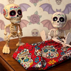 Two creepy cute statues alongside the bright red sensory fidget bag, clearly demonstrating the perfect scale and fit for these 5-inch companions. This gothic tactile sensory item decor showcases the ultimate upgrade for your ADHD fidget tool for office use. The bag adds an extra layer of tactile satisfaction to the articulated skeleton, making it a highly desirable witchy gift for friend or a quirky gift for adhd friend seeking fun dopamine decor.
