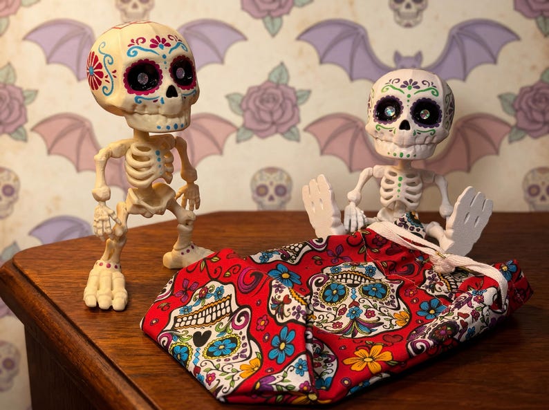 Two creepy cute statues alongside the bright red sensory fidget bag, clearly demonstrating the perfect scale and fit for these 5-inch companions. This gothic tactile sensory item decor showcases the ultimate upgrade for your ADHD fidget tool for office use. The bag adds an extra layer of tactile satisfaction to the articulated skeleton, making it a highly desirable witchy gift for friend or a quirky gift for adhd friend seeking fun dopamine decor.