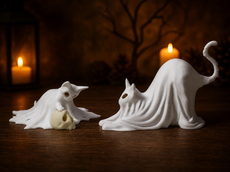The left profile of the stretching ghost cat looking at the kitten ghost with a skull, arranged as a whimsigoth Halloween decoration on a wooden table.