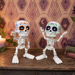 Two articulated skeletons posed in the middle of a lively, animated conversation, with one raising both hands and the other raising one. This playful scene demonstrates the extreme posability of this weirdcore desk fidget toy. A brilliant coworker gag gift and gothic tactile sensory item decor piece. This sugar skull figure is an engaging ADHD fidget tool for office desks and serves as the perfect witchy gift for friend or fun dopamine decor.