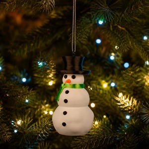 The green-scarfed snowman ornament hanging from a Christmas tree in a darkened, cozy room aglow with warm fairy lights.