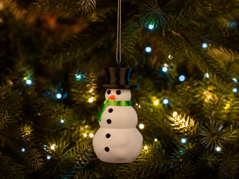 The green-scarfed snowman ornament hanging from a Christmas tree in a darkened, cozy room aglow with warm fairy lights.