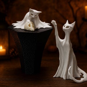 The kitten ghost cat elevated on its platform next to the tall reaching ghost cat statue, creating an eerie shelf sitter display on a rustic wooden surface.