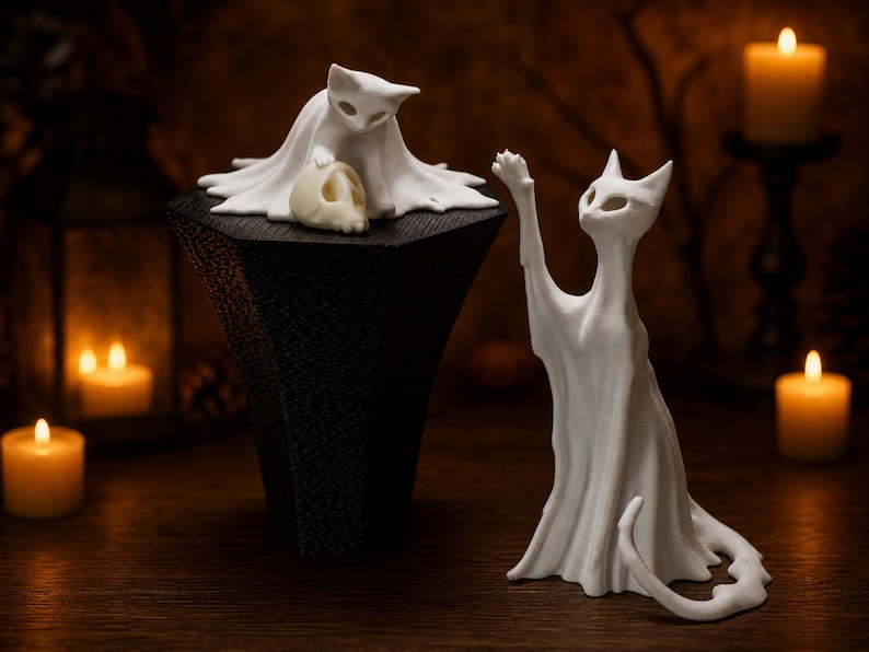 The kitten ghost cat elevated on its platform next to the tall reaching ghost cat statue, creating an eerie shelf sitter display on a rustic wooden surface.