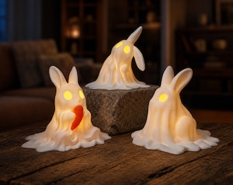 May include: Three white, glowing rabbit-shaped ghost figurines. One rabbit holds an orange carrot, one is positioned on a stone, and one sits on a wooden surface. Each figure features illuminated yellow eyes and a smooth, draped, sheet-like appearance.