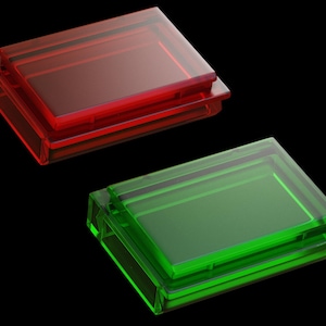 Pode incluir: Duas caixas retangulares de vidro, uma vermelha e outra verde, estão empilhadas uma em cima da outra. As caixas são translúcidas e têm um brilho ligeiro.