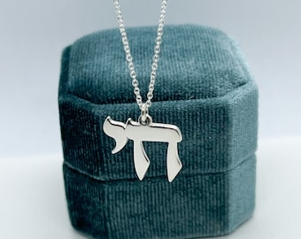 Può includere: Una collana con catena d'argento con un ciondolo d'argento a forma della lettera ebraica Chai. La collana è in una scatola per gioielli in velluto turchese.