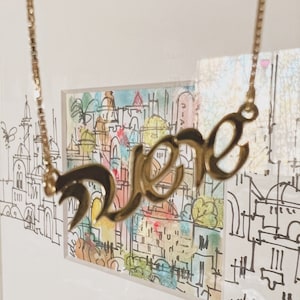 Puede incluir: Collar de oro con un colgante de nombre en escritura cursiva que dice "Love" en una fuente estilizada.