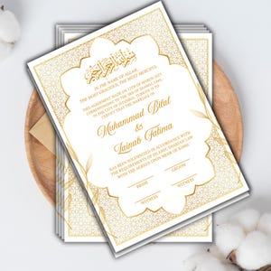 May include: Wedding invitation with gold detailing on a white background. The design includes ornate borders and Arabic calligraphy. The names Muhammad Bilal & Tainab Fatima are displayed, along with the date and location of the ceremony.