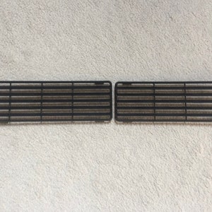 May include: Two black plastic vent grilles with horizontal slats. The grilles are rectangular and have a smooth, matte finish.