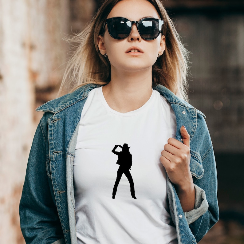 May include: A white t-shirt with a black silhouette of a woman wearing a cowboy hat and posing with her hand on her hip.
