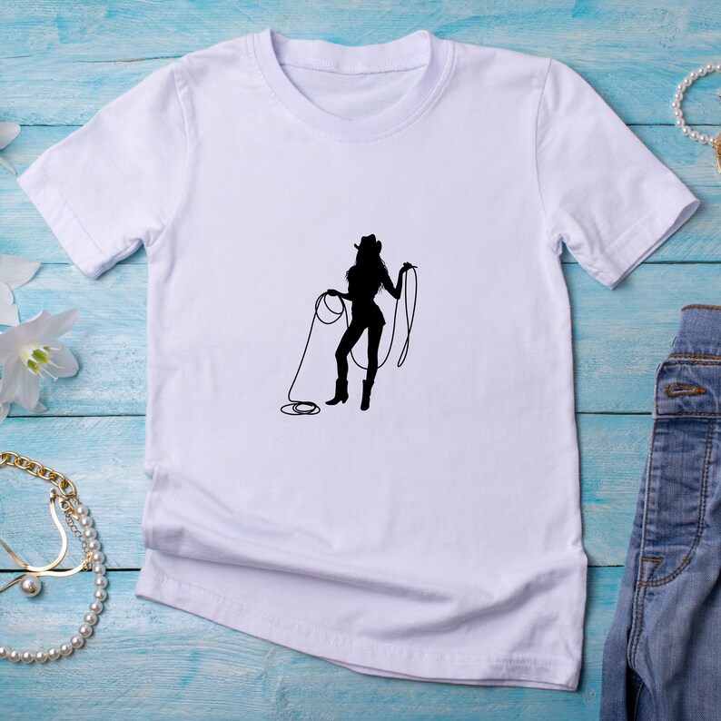 May include: White t-shirt with a black silhouette of a woman in a cowboy hat holding a lasso.