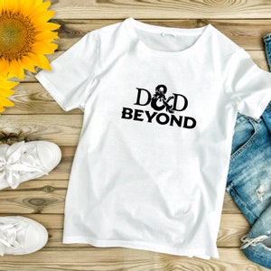 May include: White t-shirt with the text "D&D BEYOND" in black. The shirt is a crew neck style. The image also shows a pair of white sneakers, a pair of blue jeans, and a yellow sunflower.
