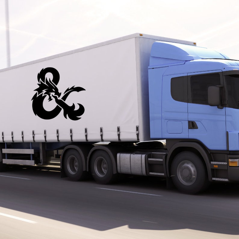 May include: A light blue semi-truck with a white trailer. The trailer features a large black graphic of a dragon intertwined with an ampersand symbol. The truck is driving on a paved road.