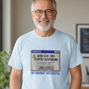 May include: A light blue t-shirt featuring a graphic of a computer error window with the text WORK.EXE HAS STOPPED RESPONDING and a button labeled END TASK. Below the window, the text RETIREMENT SUCCESSFUL is printed in blue capital letters.