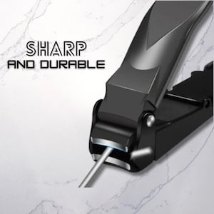 Puede incluir: Cortau&ntilde;as negro con una lima de u&ntilde;as plateada. Las tijeras tienen un dise&ntilde;o elegante y moderno con las palabras "SHARP AND DURABLE" en texto blanco. Las tijeras est&aacute;n sobre una superficie blanca y gris similar al m&aacute;rmol.
