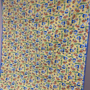 May include: A yellow baby quilt with a blue border. The quilt features a repeating pattern of blue elephants, orange flowers, and green leaves.