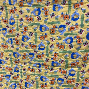 May include: A yellow fabric with a repeating pattern of blue elephants, orange lions, green alligators, and butterflies. The fabric has a quilted texture.