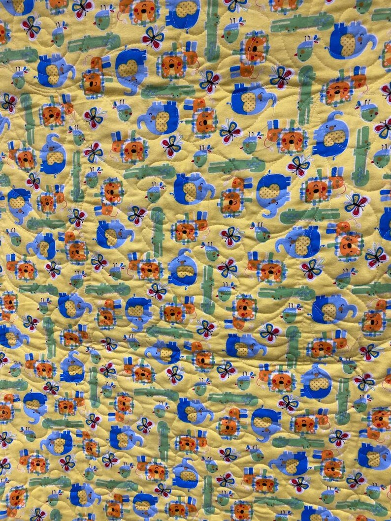 May include: A yellow fabric with a repeating pattern of blue elephants, orange lions, green alligators, and butterflies. The fabric has a quilted texture.