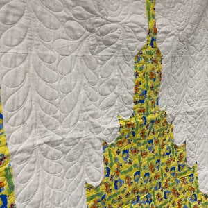 May include: A white quilt with a yellow and blue patterned fabric border. The quilt is quilted with a leaf design.