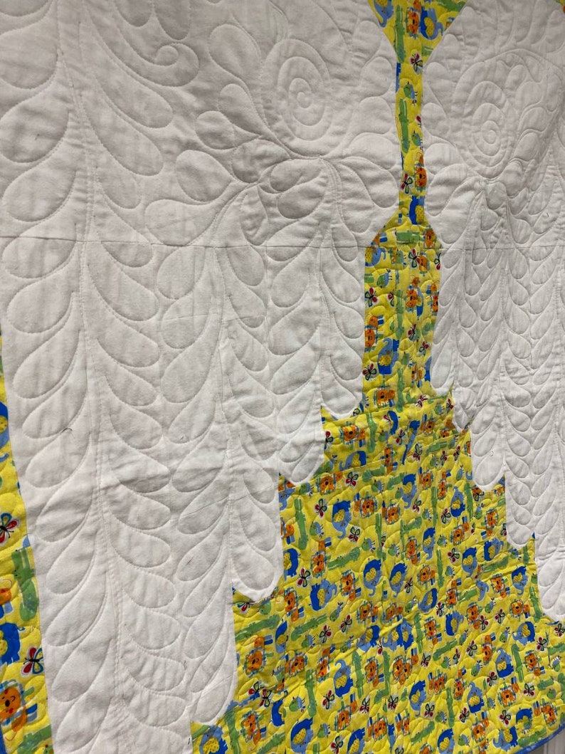 May include: A white quilt with a yellow and blue patterned fabric border. The quilt is quilted with a leaf design.