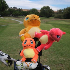 May include: Three plush toy golf club head covers featuring popular Pokemon characters. The covers are orange, yellow, and pink. The covers are in a golf bag.