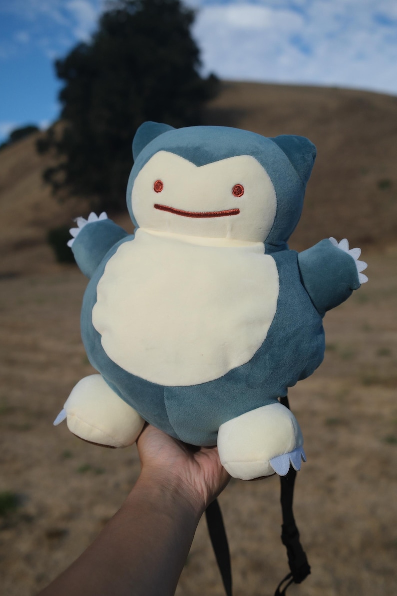 Pu&ograve; includere: Un giocattolo di peluche blu e bianco di un personaggio Pok&eacute;mon, Squirtle. Il giocattolo ha un grande sorriso ed &egrave; tenuto da una mano.
