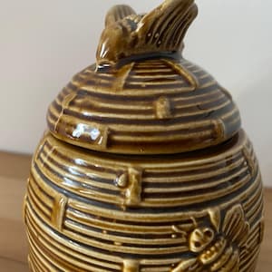May include: A brown ceramic honey pot shaped like a beehive with a bee on top of the lid.