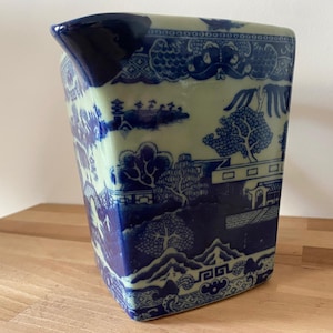 May include: A blue and white ceramic jug with a traditional Chinese design. The jug has a square shape and a wide mouth.
