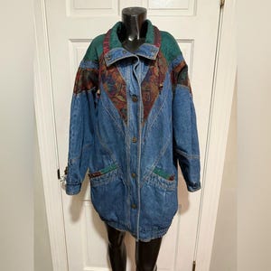 May include: A vintage denim jacket with a unique design. The jacket features a blue denim body with colorful patterned panels on the shoulders and chest. It has a green collar and accents, and is buttoned down the front.
