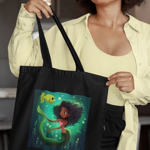 May include: Black tote bag with a green mermaid and a yellow fish illustration. The mermaid has long black hair and is wearing a pink seashell bra.