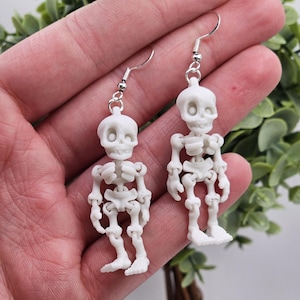 May include: A pair of white skeleton earrings. The skeletons are detailed and have a realistic look. The earrings are made of polymer clay and are lightweight and comfortable to wear.